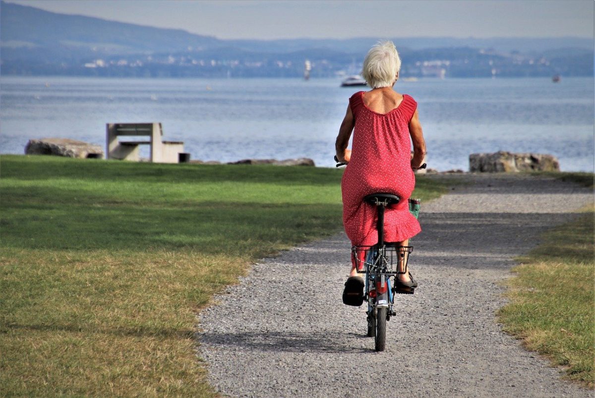 photo of senior lady in red riding a bicycle near the harbor for story There Goes Mama by JeniseCook.com